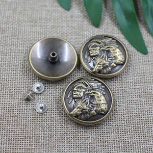 May include: Three antique brass-colored metal buttons with a Native American chief and wolf design. The buttons have a detailed relief and are accompanied by silver rivets for attachment. The buttons are round and have a vintage aesthetic.