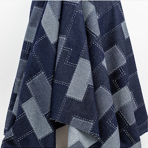 Puede incluir: Una tela vaquera azul oscuro con un diseño de patchwork. La tela está hecha de diferentes tonos de mezclilla azul y está cosida en un patrón geométrico.