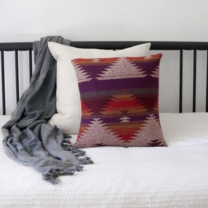 May include: A white bed with a black metal headboard and a gray throw blanket. A patterned pillow with red, orange, purple, and brown colors is on the bed.