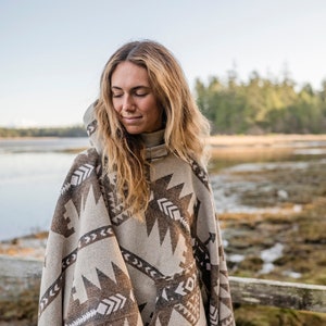 Puede incluir: Una mujer lleva un poncho con capucha con un patr&oacute;n geom&eacute;trico marr&oacute;n y blanco. El poncho est&aacute; hecho de una tela suave y tejida y tiene un corte holgado.