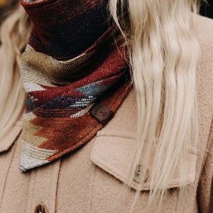 May include: A close-up of a woman wearing a brown jacket with a colourful patterned bandana tied around her neck. The bandana has a small leather tag with a logo on it.