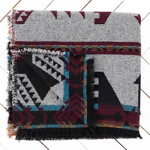 May include: A woven throw blanket with a geometric pattern in shades of gray, black, burgundy, teal, and gold. The blanket has a fringed edge.