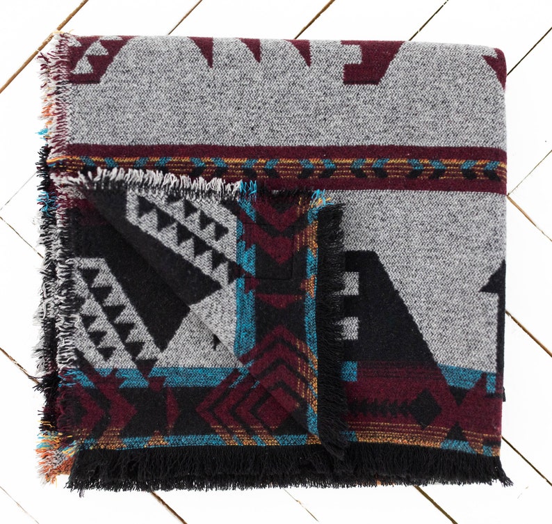 May include: A woven throw blanket with a geometric pattern in shades of gray, black, burgundy, teal, and gold. The blanket has a fringed edge.