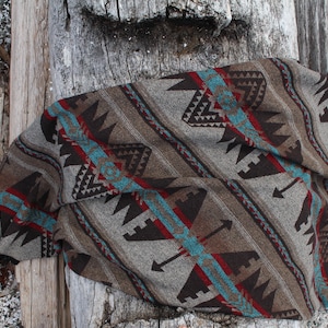 May include: A brown, turquoise, and red patterned throw blanket with a southwestern design. The blanket is folded and lying on a wooden surface.