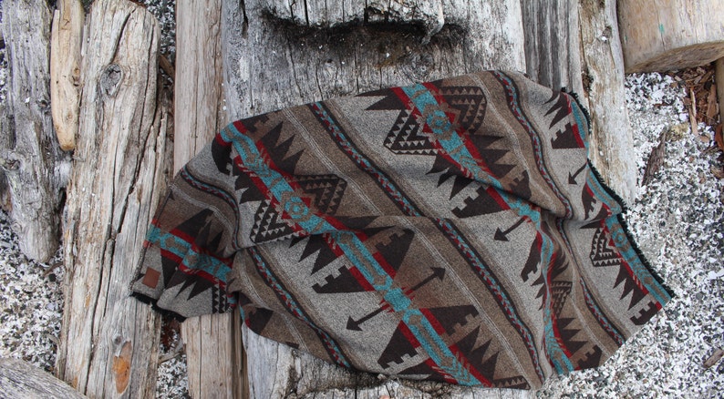 May include: A brown, turquoise, and red patterned throw blanket with a southwestern design. The blanket is folded and lying on a wooden surface.
