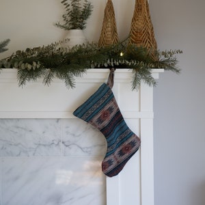 May include: A blue and brown patterned Christmas stocking hangs from a white mantel above a marble fireplace.