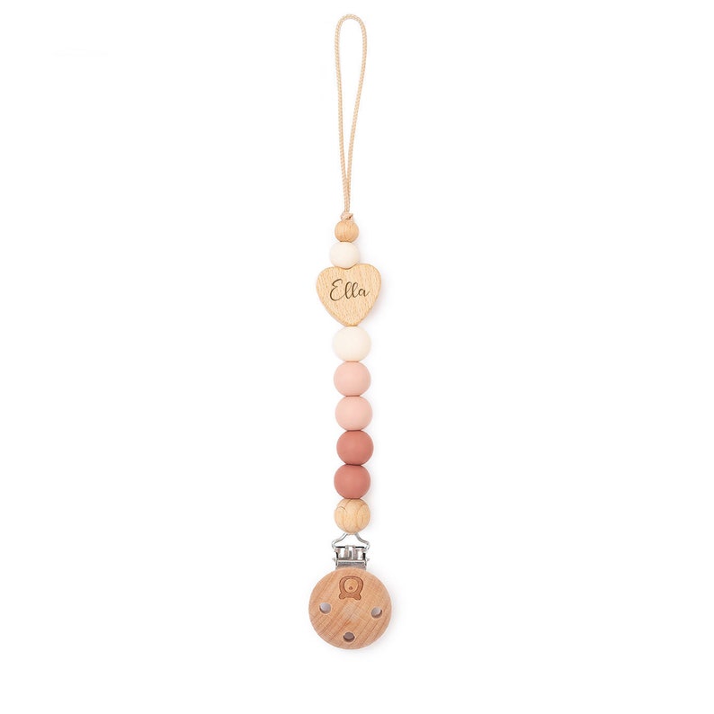 Op de afbeelding: Een houten en siliconen baby-bijtje met een hartvormige hanger waarop "Ella" staat. De bijtje heeft een clip om aan kleding te bevestigen.