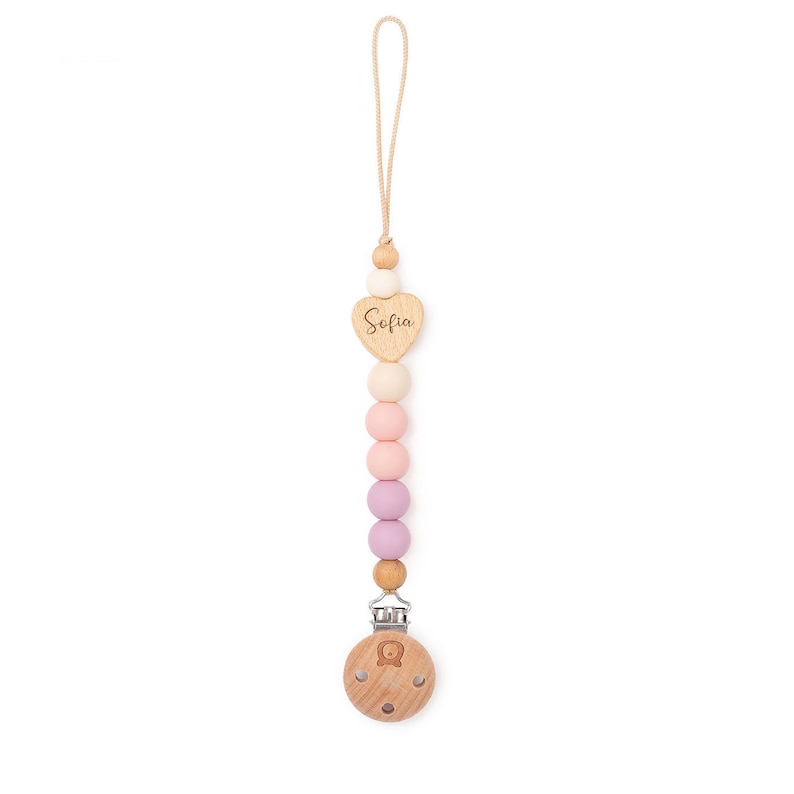 Op de afbeelding: Een houten baby-bijtje met een hartvormige hanger waarop "Sofia" staat. De bijtje heeft een roze, witte en beige kleurstelling en is bevestigd aan een clip.