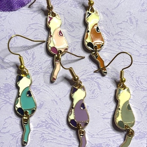 May include: A collection of five cat-shaped dangle earrings. Each earring features a gold-colored hook and a cat silhouette with colorful enamel details. The cats have various color combinations, including white, pink, and blue.