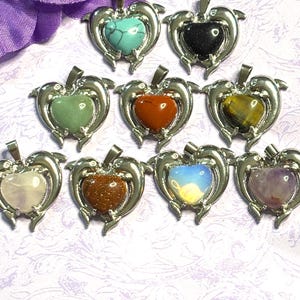 May include: A collection of heart-shaped pendants with various gemstones, including turquoise, black, green, red, yellow, white, brown, opalescent, and purple. Each pendant is framed by a silver-colored dolphin design and includes a silver chain.