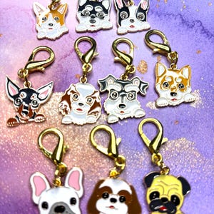 May include: A collection of dog-themed charms with gold-colored clasps. The charms feature various dog breeds, including a corgi, husky, and pug, in enamel with black, white, brown, and yellow coloring. The background is a purple and gold marbled pattern.