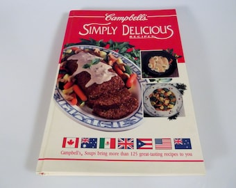 May include: A cookbook titled "Campbell's Simply Delicious Recipes" with a red cover and a photo of a meatloaf with gravy and vegetables on the front. The book features a variety of international flags on the bottom.