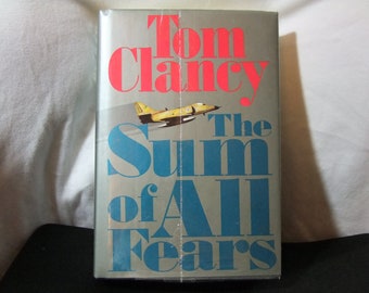 Könnte beinhalten: Ein Buchcover mit silbernem Hintergrund und dem Titel "The Sum of All Fears" in blauer Schrift. Der Name des Autors, "Tom Clancy", ist in roter Schrift. Ein gelbes und schwarzes Kampfflugzeug fliegt im Hintergrund.