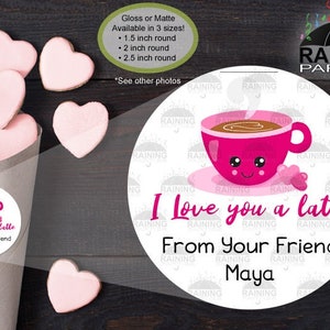 May include: A round sticker with a pink cartoon coffee cup with a smiling face and the text "I love you a latte" and "From Your Friend Maya". The sticker is on a brown background with pink heart-shaped cookies.