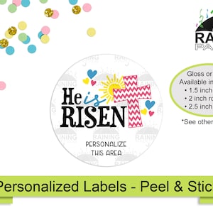 May include: Round sticker with a white background and a pink and white chevron cross with a yellow sun and blue hearts. The text "He is RISEN" is in black. The sticker is available in 1.5, 2, and 2.5 inch sizes.