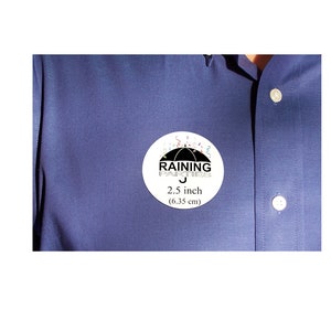 Puede incluir: Una pegatina redonda blanca con un paraguas negro y el texto "RAINING FOR SUCCESS" en negro. La pegatina tambi&eacute;n tiene confeti de colores alrededor del paraguas y el texto "2,5 pulgadas (6,35 cm)".