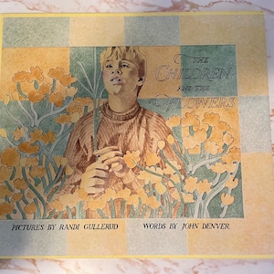 Op de afbeelding: Een boekomslag met een gele, groene en bruine geruite achtergrond. De omslag toont een jonge jongen die een boeket gele bloemen vasthoudt. De titel van het boek is "The Children and the Flowers". Het boek is van Randi Gullerud en John Denver.