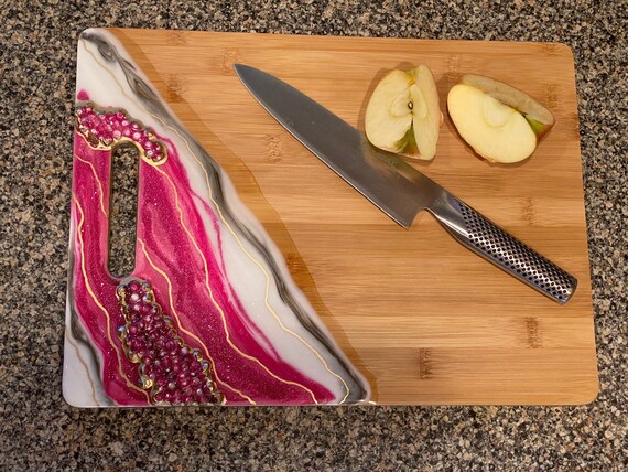 Hand poured resin bamboo cheese/cutting board in marble fuchsia,white, and gold glitter accented with acrylic gems 15x11.5 trimmed in gold