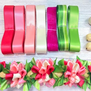 May include: A collection of colorful ribbons in shades of red, pink, green, and white, along with wooden beads and a floral lei. The ribbons are neatly stacked, showcasing their vibrant hues. The lei features pink and red flowers with green leaves.
