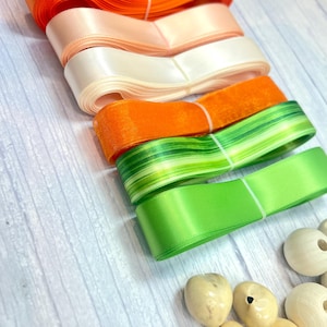 Peut inclure: Rubans de satin color&eacute;s, orange, p&ecirc;che, blanc et vert. Les rubans sont enroul&eacute;s et attach&eacute;s avec de la ficelle blanche. Des perles en bois sont &eacute;galement visibles, sugg&eacute;rant un th&egrave;me artisanal.