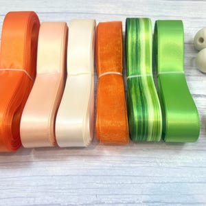 Peut inclure: Une collection de rubans color&eacute;s dans les tons orange, p&ecirc;che, cr&egrave;me et vert. Les rubans sont soigneusement regroup&eacute;s et dispos&eacute;s &agrave; c&ocirc;t&eacute; de perles en bois. Les rubans sont en satin et autres mat&eacute;riaux, parfaits pour l'artisanat et les d&eacute;corations.