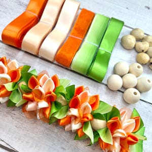 Peut inclure: Un assortiment de fournitures de bricolage comprenant des rubans de satin orange, cr&egrave;me et vert, des perles en bois et une garniture de ruban floral. La garniture florale pr&eacute;sente des fleurs et des feuilles en ruban de satin orange, cr&egrave;me et vert.
