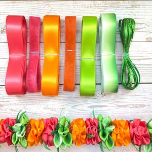May include: Assortment of colorful ribbons and a floral garland. The ribbons include shades of red, orange, green, and a shimmering green cord. The garland features red and orange fabric flowers with green leaves, perfect for crafting or decoration.