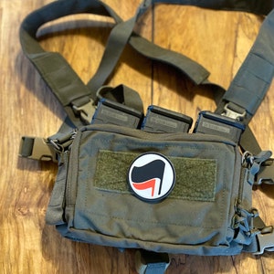 May include: A green tactical chest rig with three black magazine pouches and a black and red anarchist symbol patch.