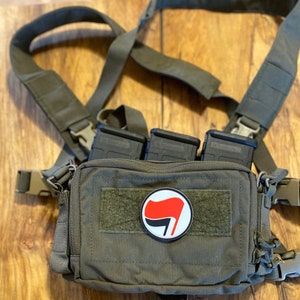 May include: A green tactical chest rig with three black magazine pouches and a red and black anarchist symbol patch.