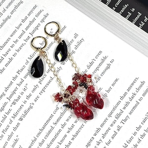 May include: A pair of earrings featuring a gold chain and red and black glass beads. One earring has a black teardrop-shaped bead and the other has a cluster of red beads shaped like hearts.