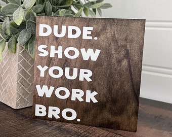 May include: A wooden sign with the text "DUDE. SHOW YOUR WORK BRO." in white letters on a dark brown background.