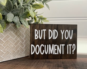 May include: A dark brown wooden sign with white text that reads "But did you document it?"