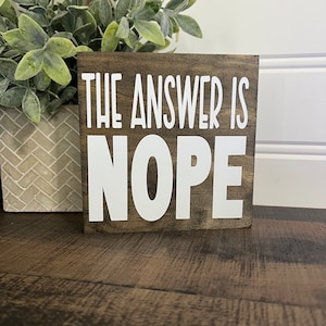 May include: A wooden sign with the text "THE ANSWER IS NOPE" in white letters on a brown background.