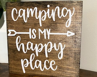 May include: A wooden sign with the text "camping is my happy place" in white lettering. The sign has a white arrow pointing to the right.