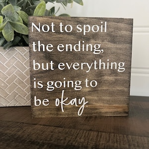 May include: A wooden sign with the text "Not to spoil the ending, but everything is going to be okay." The sign is brown with white lettering.