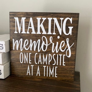 May include: A brown wooden sign with white text that reads "Making memories one campsite at a time".