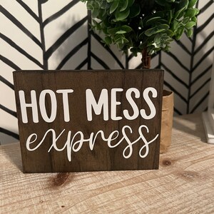 May include: A brown wooden sign with white lettering that reads "HOT MESS express".