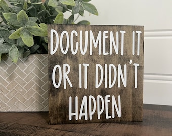 May include: A small wooden sign with a brown stain and white lettering. The sign reads "Document it or it didn't happen."