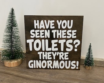 May include: A wooden sign with the text "Have you seen these toilets? They're ginormous!" in white lettering on a dark brown background.