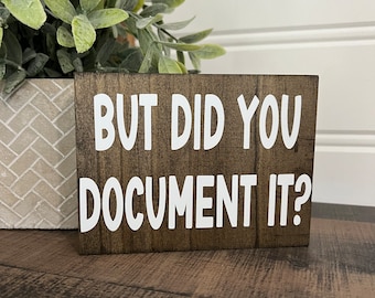 May include: A brown wooden sign with white text that reads "But did you document it?"