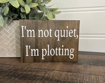 Może przedstawiać: Drewniany znak z napisem "I'm not quiet, I'm plotting" w białych literach.