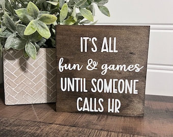 May include: A brown wooden sign with white text that reads "It's all fun & games until someone calls HR".