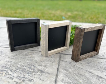 May include: Three square wooden frames with black chalkboard inserts. The frames are in different wood stains: black, gray, and brown.