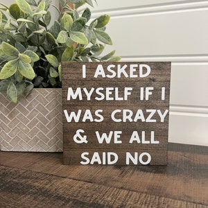 May include: Wooden sign with the text "I asked myself if I was crazy & we all said no" in white letters.