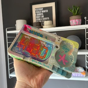 May include: A white ceramic mug with a black handle and the text "But First, Coffee" in a black, bold font. The mug is sitting on a wooden surface.