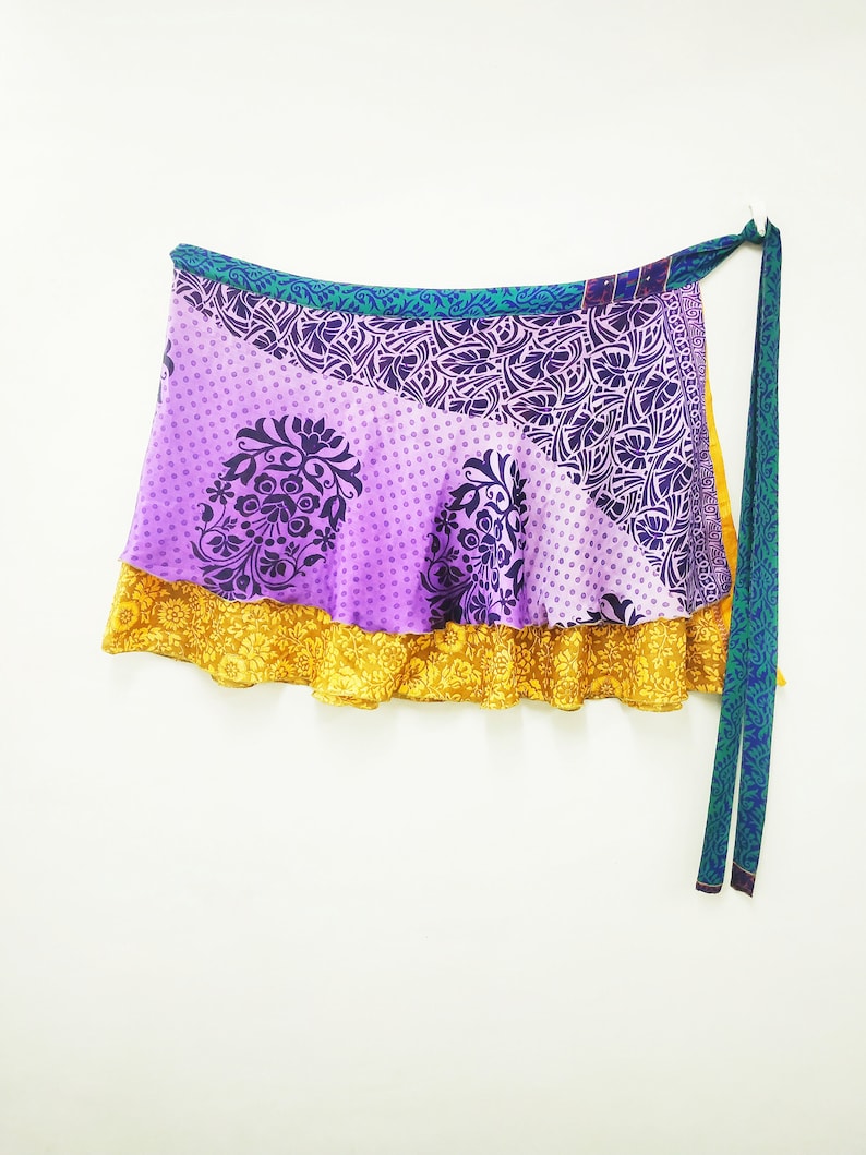 May include: A multi-layered wrap skirt with a purple, yellow and green floral print. The skirt is tied with a long green sash.