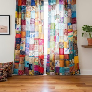 Op de afbeelding: Patchwork gordijnen in diverse kleuren, waaronder rood, geel, blauw en groen. De gordijnen zijn gemaakt van aan elkaar genaaide stoffen vierkanten. De gordijnen hangen aan een roede met bordeauxrode stoffen lussen.