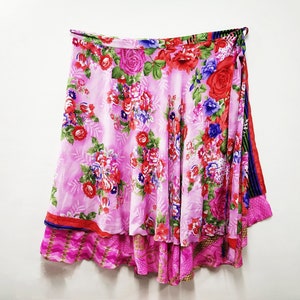 Könnte beinhalten: Ein rosa Wickelrock mit Blumenmuster. Der Rock hat einen mehrfarbigen Saum und einen Bindegürtel an der Taille.