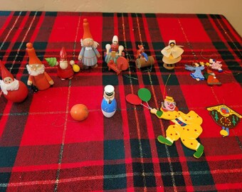 May include: A collection of 14 wooden Christmas ornaments, including a Santa Claus, a clown, a gnome, a carousel horse, and a cuckoo clock. The ornaments are painted in bright colors and have a whimsical, vintage style.