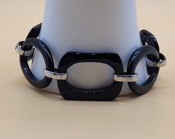 May include: A black and silver bracelet with large, rounded, black links. The bracelet is made of a smooth, shiny material.